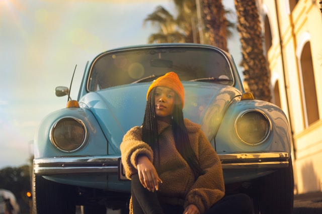 Žena v oranžovej čiapke sedí pred modrým autom