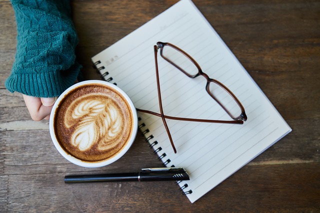 Notes, okuliare a žena drží v ruke šálku s kávou